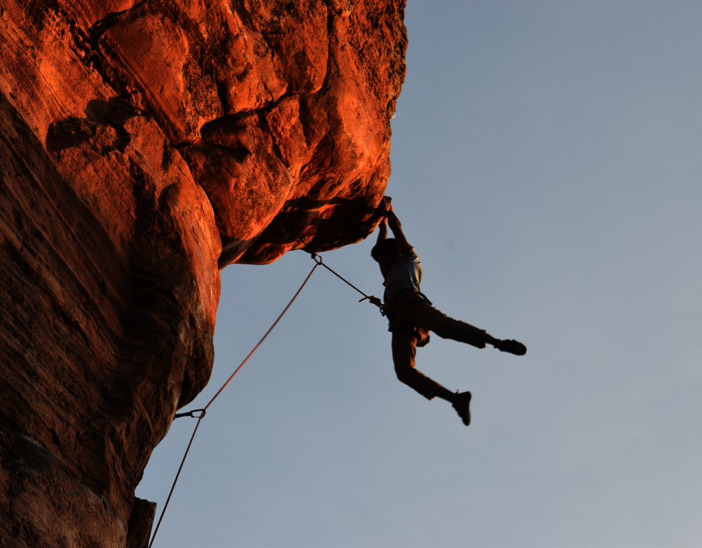 Person climbing the side of a cliff, holding on with their feet hanging.