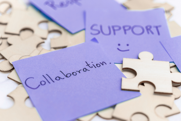 An array of wooden puzzle pieces with post-it notes on top with the word "Collaboration" written on one of the notes, and "SUPPORT" with a smiley face on the other.