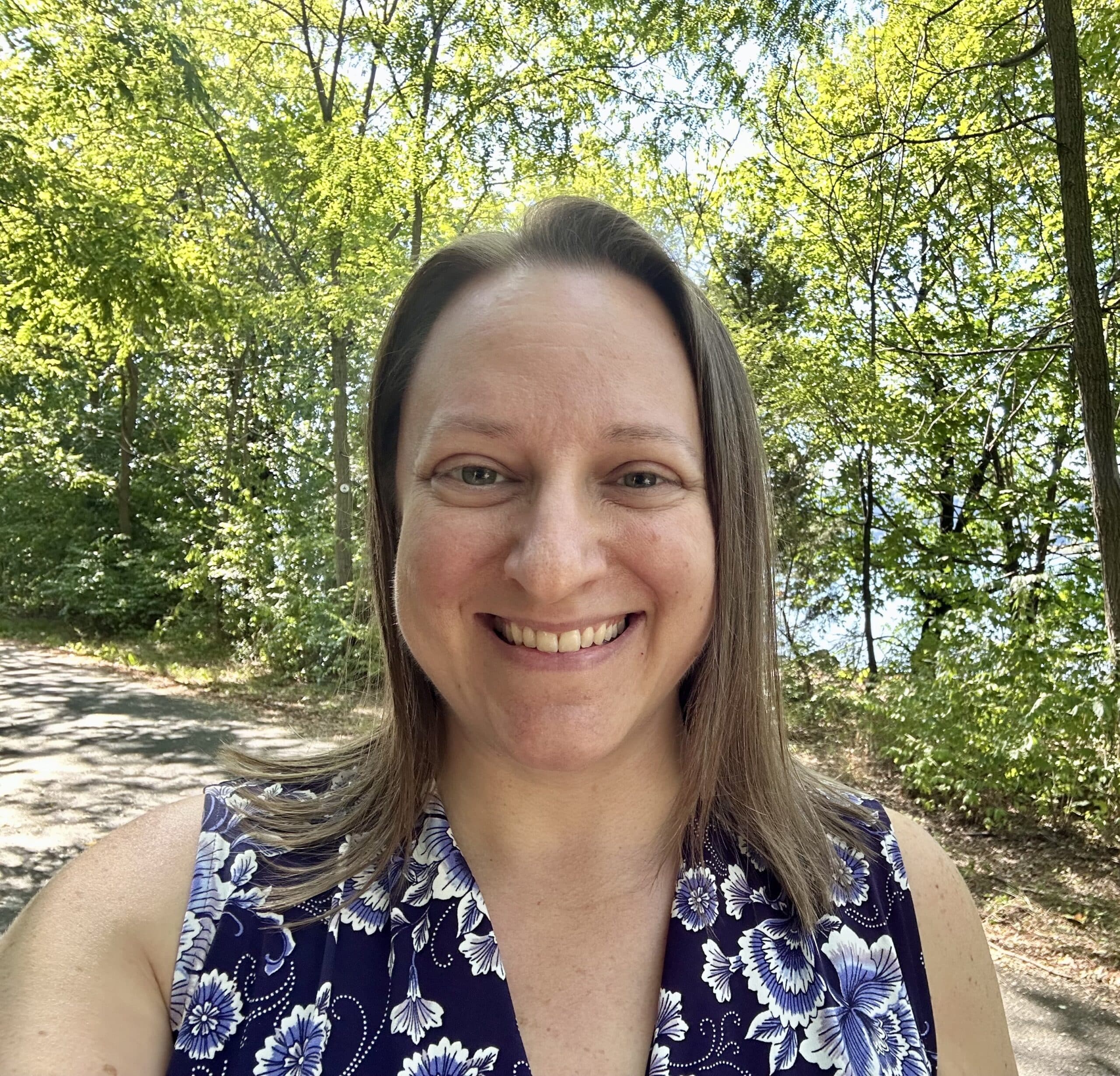 Headshot of mindfulness coach, Robyn Gold, standing on a path in nature with trees and water in the background.